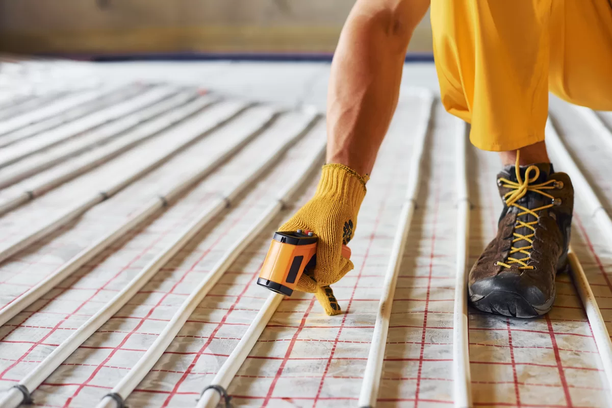 measures heat of the pipes. worker in yellow colored uniform installing underfloor heating system